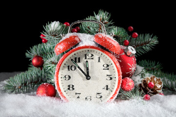 Fototapeta na wymiar Vintage alarm clock with fir twigs, cones, red trinkets and berries. Time ten to midnight. Black background with snow. Merry Christmas, Happy New Year.