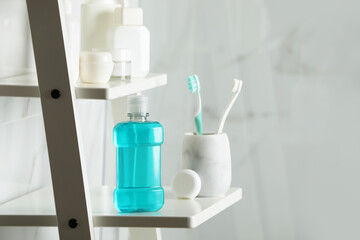 Bottle of mouthwash, toothbrushes and dental floss on white shelf in bathroom