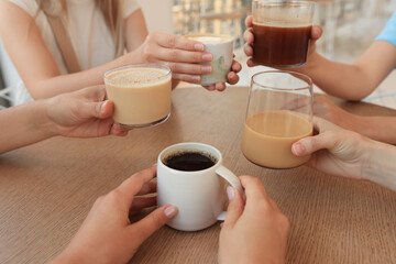 Friends drinking coffee at wooden table in cafe, closeup