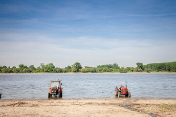 .Two vintage old tractors on a beach on the riverbank of the danube river with a panorama over it...