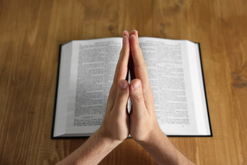 Naklejka premium Man with Bible praying at wooden table, closeup