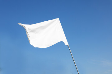 White flag fluttering against blue sky on sunny day