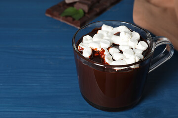 Glass cup of delicious hot chocolate with marshmallows on blue wooden table. Space for text