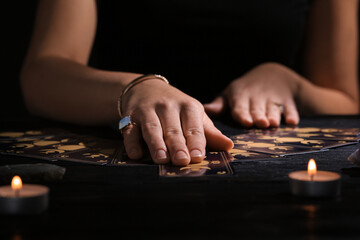 Soothsayer predicting future with tarot cards at table in darkness, closeup