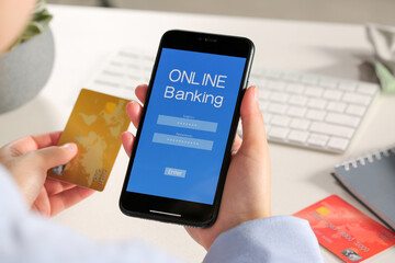 Woman using online banking app on smartphone and credit card at white office table, closeup