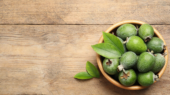 Fresh green feijoa fruits in bowl on wooden table, top view with space for text. Banner design