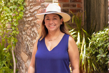 Latina morena con sombrero, sonriendo en una fachada del pueblo