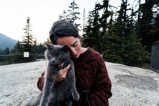Young woman holds her gray russian blue cat and give her loves out in wilderness forest.