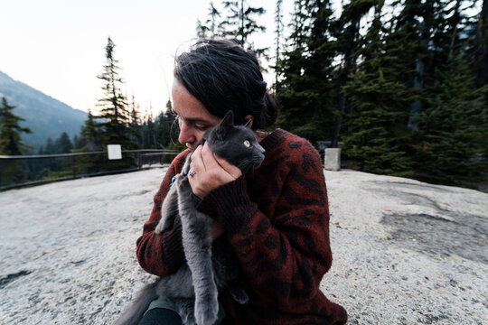 Young woman holds her gray russian blue cat and give her loves out in wilderness forest.
