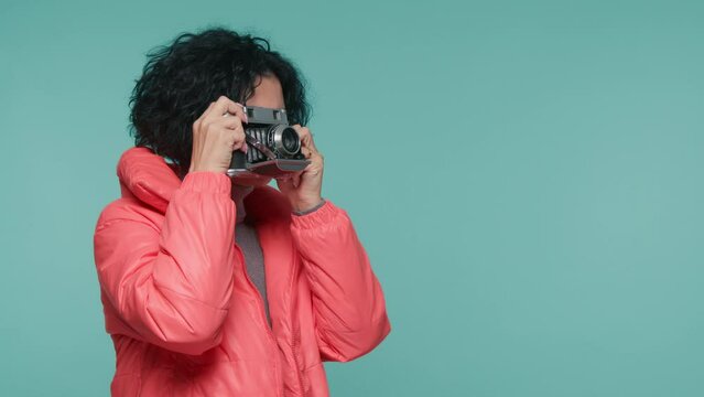 Happy woman 40s with photo camera standing in warm jacket on pastel blue background. Female photographer taking photos on film camera. Mature woman looking pictures on analog camera, Travel concept 4K