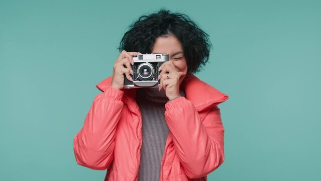 Mature woman looking pictures on analog camera, Travel concept 4K. Happy woman 40s with photo camera standing in warm jacket on pastel blue background. Female photographer taking photos on film camera