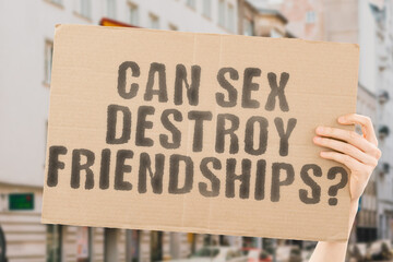 The question " Can sex destroy friendships? " is on a banner in men's hands with blurred background. Person. Man. Woman. Couple. Male. Young. Together. Feelings. Flirting. Touch. Talk. Seduce