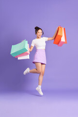Young Asian woman holding shopping bag on purple background