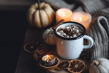 Autumn cozy home composition with hot chocolate with marshmallow and candles. Aromatherapy on a grey fall morning, atmosphere of cosiness and relax. Wooden background, window sill, close up.