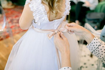 A woman's hands tying the bow on a flower girl's dress