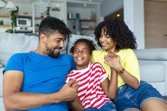 Multi-ethnic family sitting on couch in living room at home enjoy free time together on weekend communicating with each other. Beautiful daughter embrace mother has fun with parents indoors