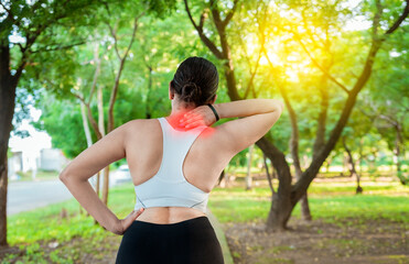 Running woman with shoulder muscle pain in a park. Shoulder pain concept of a runner athlete. Athlete girl in pain rubbing her shoulder outdoors. Back view of sporty woman with shoulder pain