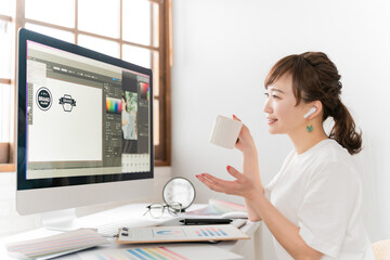 Obraz na płótnie Canvas イヤホンを使ってオンラインミーティング・WEB会議するデザイナーのアジア人女性 