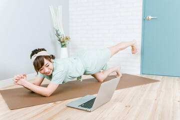 家でパソコンを見ながら筋トレする女性（プランク）

