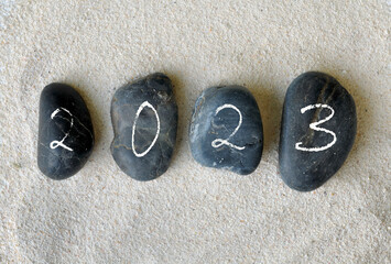 2023 written on black pebbles on the sand background