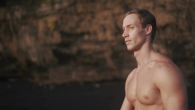 Young Caucasian man with sharp cheekbones walking at the beach, looking to the camera. Beautiful man with masculine chin and wide neck glance to the camera. Concept of man's beauty. 