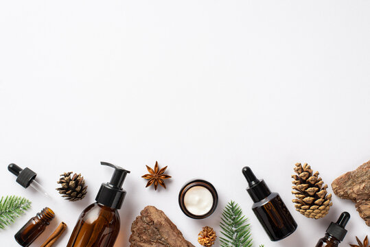 Organic skincare cosmetics concept. Top view photo of amber glass bottles fir branches pine bark cones and anise on isolated white background with copyspace