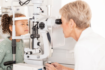 Fototapeta na wymiar Optometry, vision and optometrist doing eye test on girl for optical care, wellness and health. Senior optician doing optic examination on child with autorefractor equipment in eyewear clinic or shop