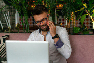 Portrait of smiling man with beard sitting with laptop, talking on phone
