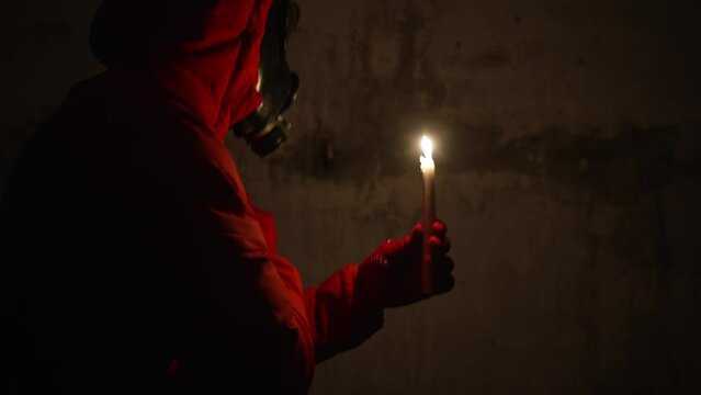 Ukraine war. Shelter. Bunker, nuclear war, a man in a gas mask and protective clothing is hiding in a bomb shelter, electricity is turned off, a man is lighting a candle, he is scared