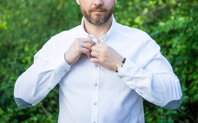 Professional unshaven guy crop view buttoning shirt natural background