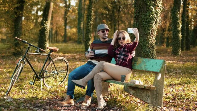 Young couple is having fun outdoors in an autumn park. They use the phone to take pictures for social media and fun