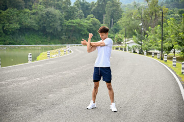 Fit and active young Asian man in sportswear starching his arms and body before running.