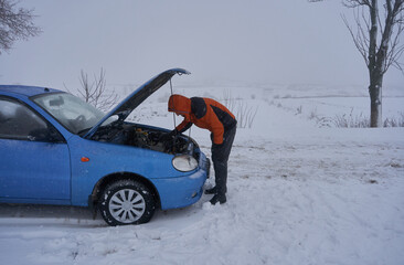 a man repairs a car in winter,a man opened the hood of a car and examines the engine, a car breakdown in winter, a blizzard and a broken car