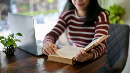 Happy Asian female college student reading a book while relaxing in the coffee shop