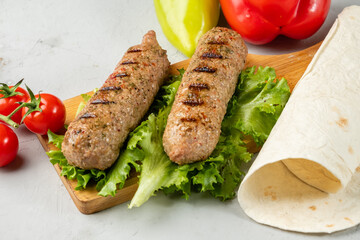 Lula kebab next to a piece of pita bread on a light background.