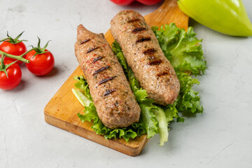Lula kebab on a wooden board with lettuce leaves and cherry tomatoes and a light background.