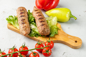 Delicious grilled soy sausages lie on a wooden board next to lettuce and cherry tomatoes. Lula...