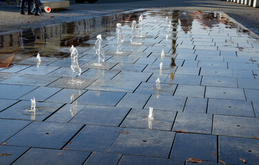 square granite paving stacked in a strip in sidewalk,boy, water sprays with alternating spray...