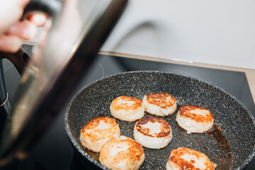 The process of toasting the cheesecakes in a pan with the lid open on an induction stove. Preparing breakfast, selective focus