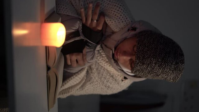 power outage and heating concept. Energy crisis in Europe. Young man reading a book by candlelight feeling cold in the house in winter