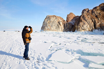 A man travels on the ice of the frozen Lake Baikal and enjoys the beautiful landscape. Huge rocks of the north of Olkhon Island. Winter travel