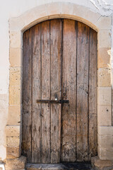 Old shabby wooden door with rusted metal latch and lock in natural stone doorway 