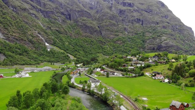 Aerial: Fl&aring;m train going through a valley among green meadows and by a river and a waterfall