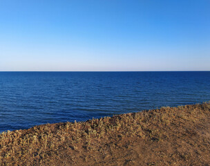 High seashore, brown clay soil overgrown with grass and meadow plants. Sea landscape.