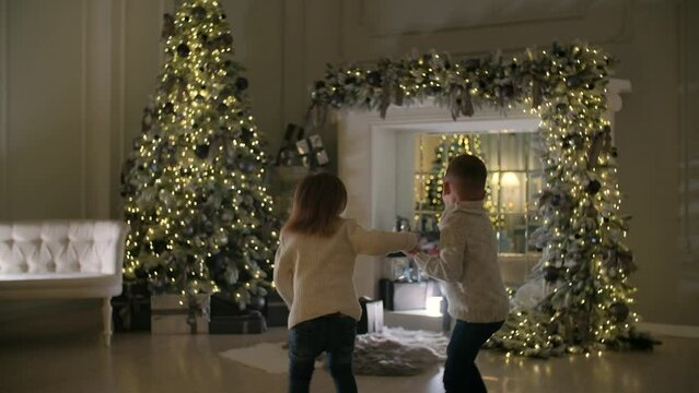 Happy children open a gift under the Christmas tree. The house is decorated with New Year's lights.