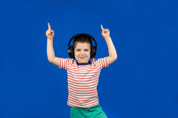 Happy boy in headphones and t-shirt points his fingers up on a blue background