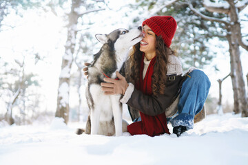 Young woman walking her dog in the winter and both explore the snow together in playful mood. Friendship, pet and human.