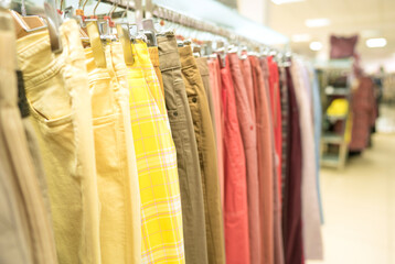 Trousers on hangers - clothing rental or reselling concept. Thrist shopping or seconhand store concept. Clothes stall against blurred store background with copy space