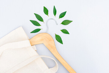Wooden hangers, white cotton bag and green leaves over light gray background with copy space. Eco...