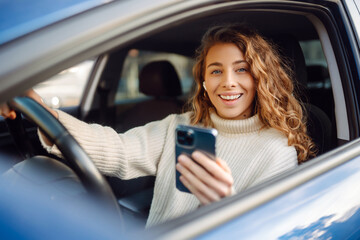 Portrait of a young woman texting on her smartphone while driving a car. Car sharing, rental...